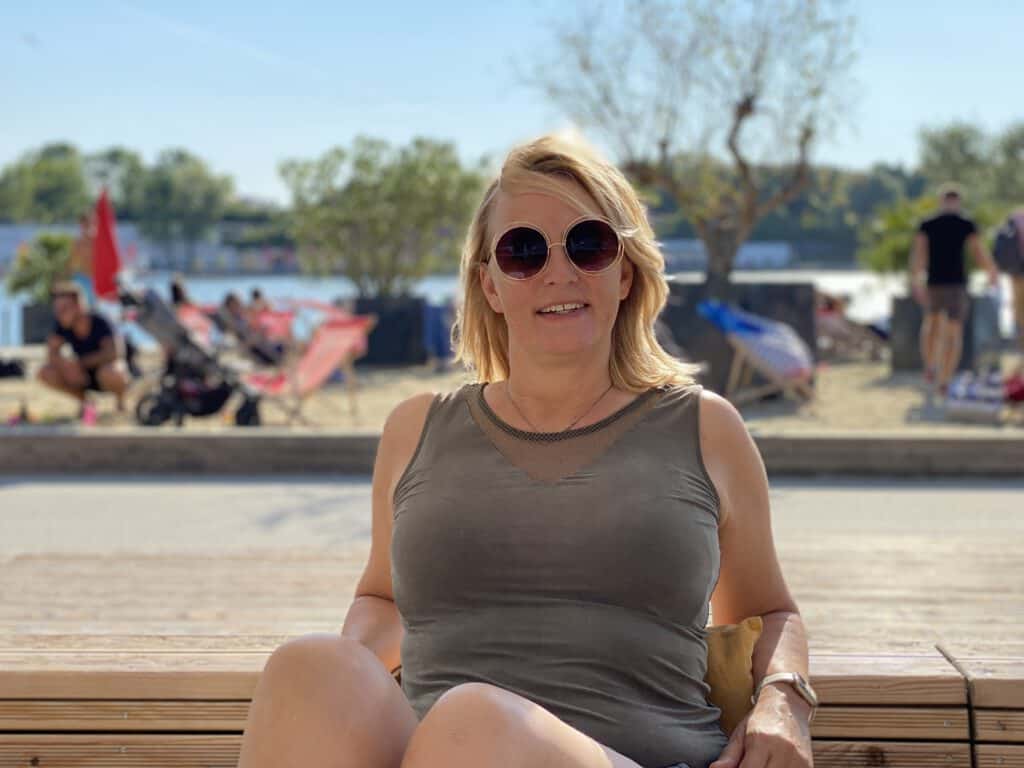 Vrouw met zonnebril geniet van de zon op het strand bij de rivier.