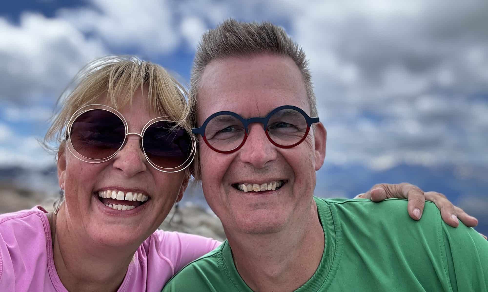 Gezellige stel mensen met grote glimlachen en zonnebrillen, genieten van de buitenlucht in de bergen.