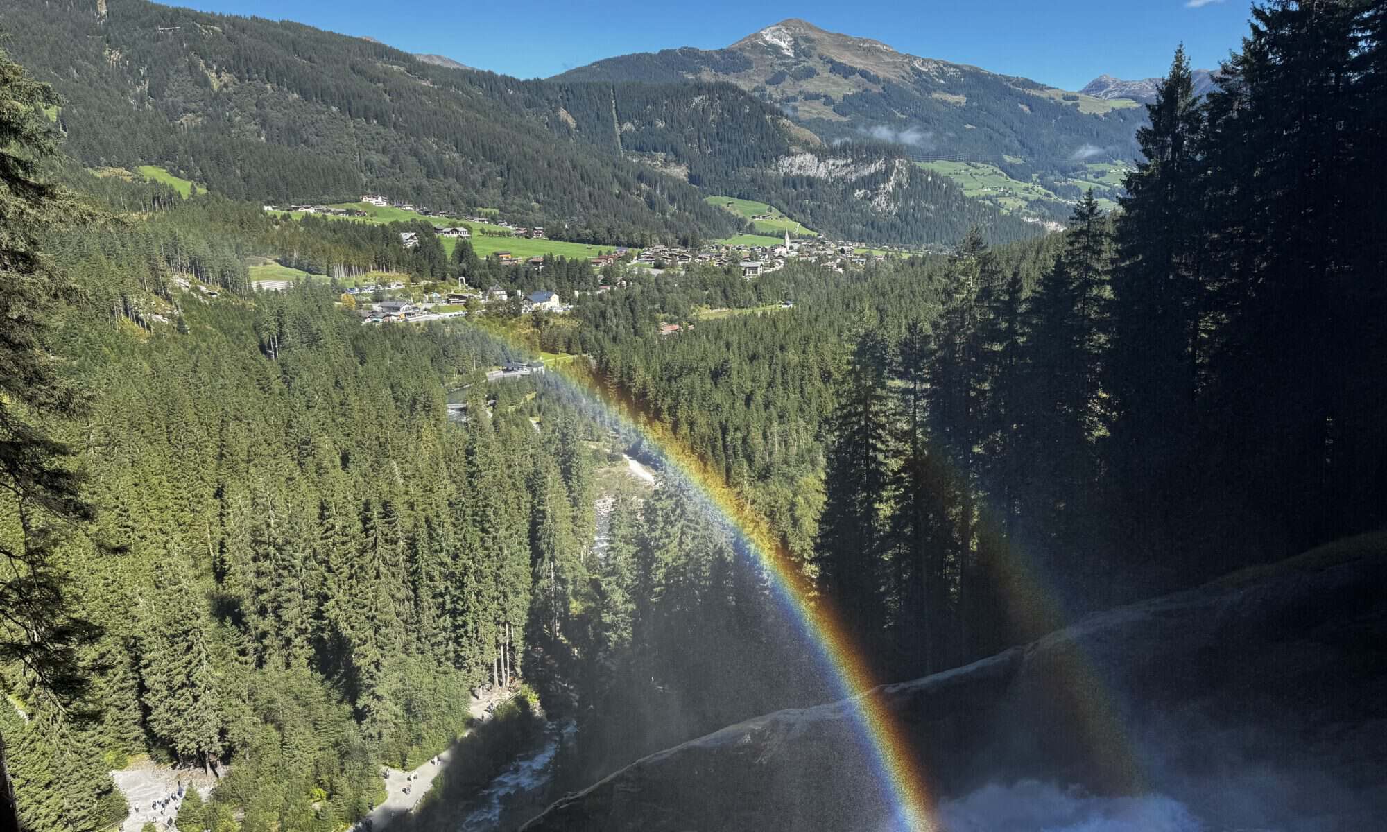 Blick op de Krimmler Wasserfälle met regenboog en berglandschap.